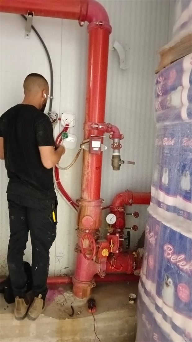 טכנאי מתקין רגש זרימה על צנרת מתזים אדומה